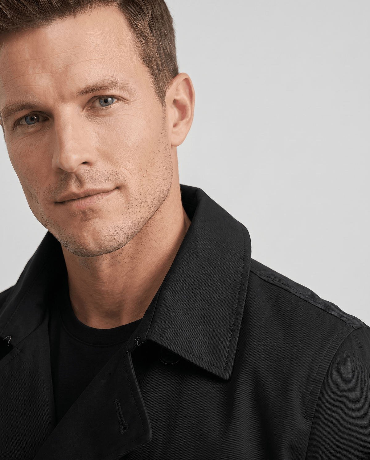 Close-up of a man wearing a black double-breasted trench coat, showing the notched lapel and collar