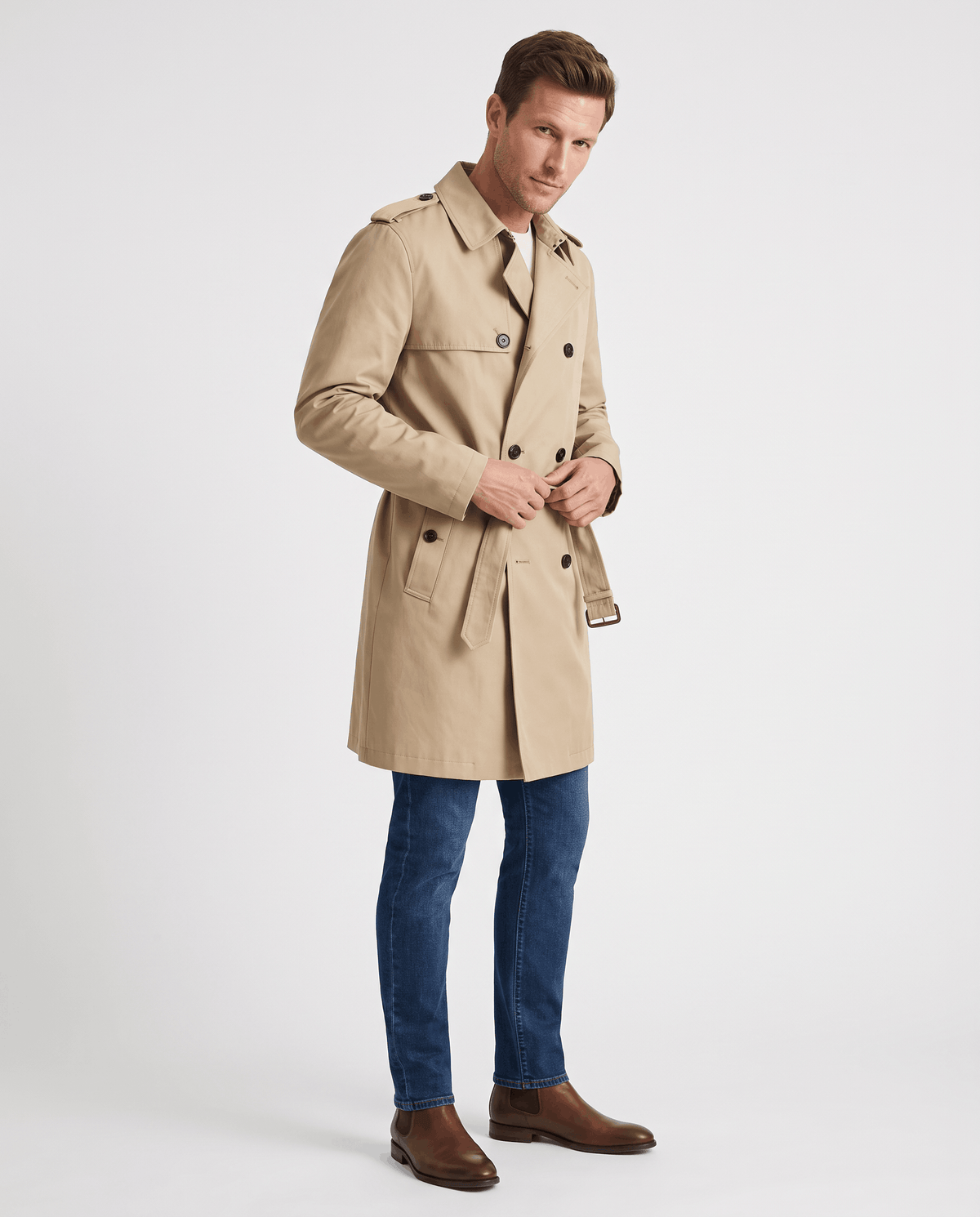 A man wearing a beige double-breasted trench coat with a mid-length fit, notched lapel, and adjustable cuffs, side view