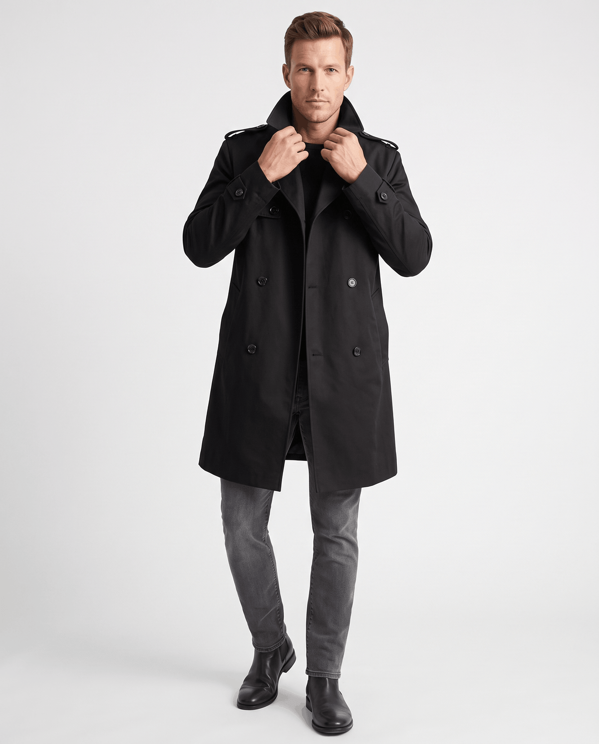 A man wearing a black double-breasted trench coat with a mid-length fit, notched lapel, and adjustable cuffs