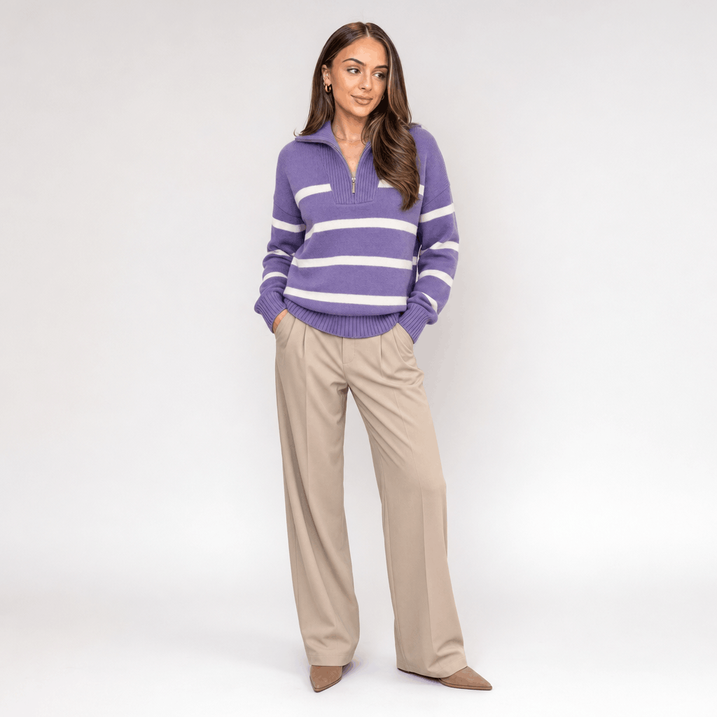 Full-body view of a female model wearing the purple and white striped quarter-zip sweater with beige trousers.