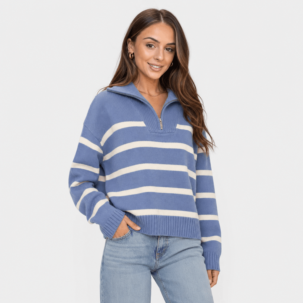 Female model wearing a blue quarter-zip sweater with white horizontal stripes, paired with light blue jeans.