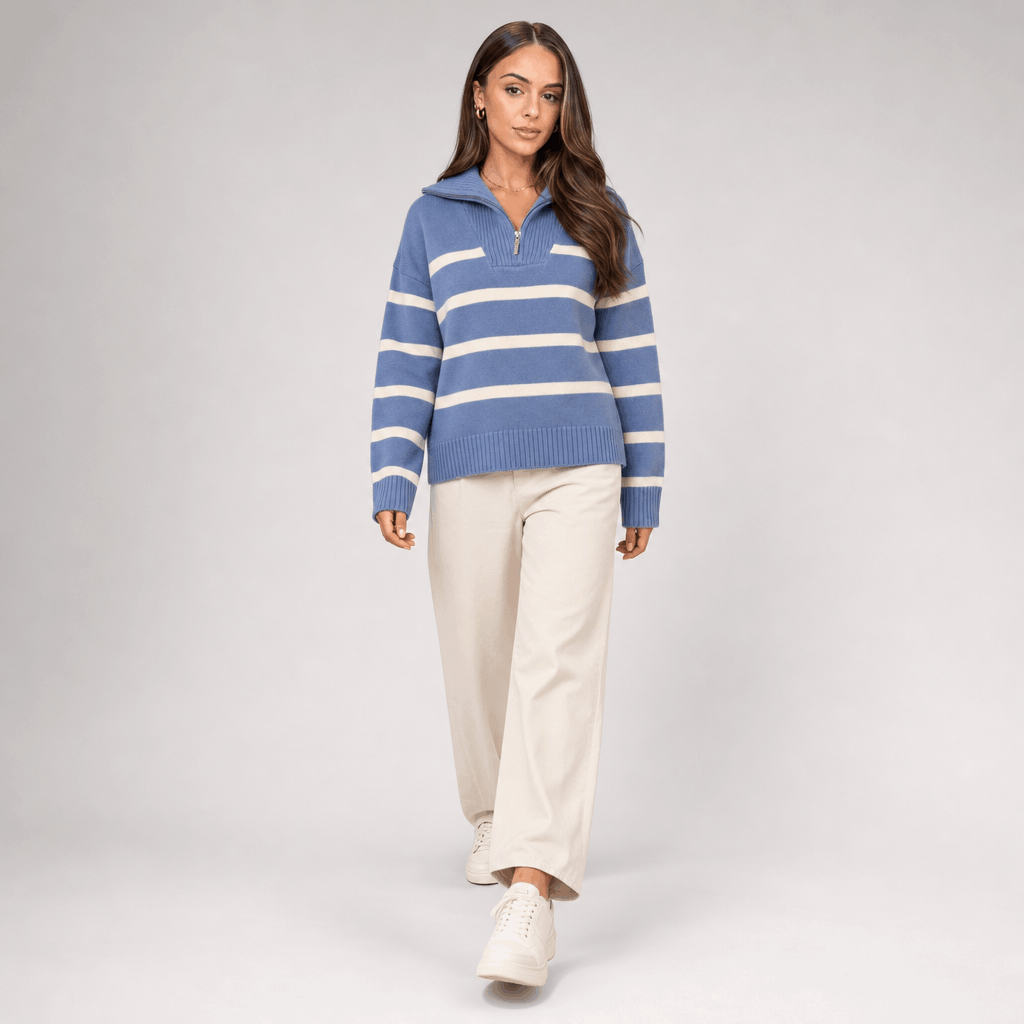 Full-body view of a female model wearing the blue and white striped quarter-zip sweater with white trousers.