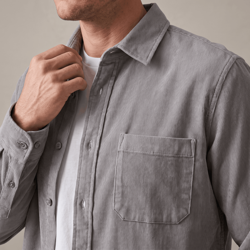 Faded grey washed corduroy button-up shirt with a single chest pocket, worn open over a white t-shirt.