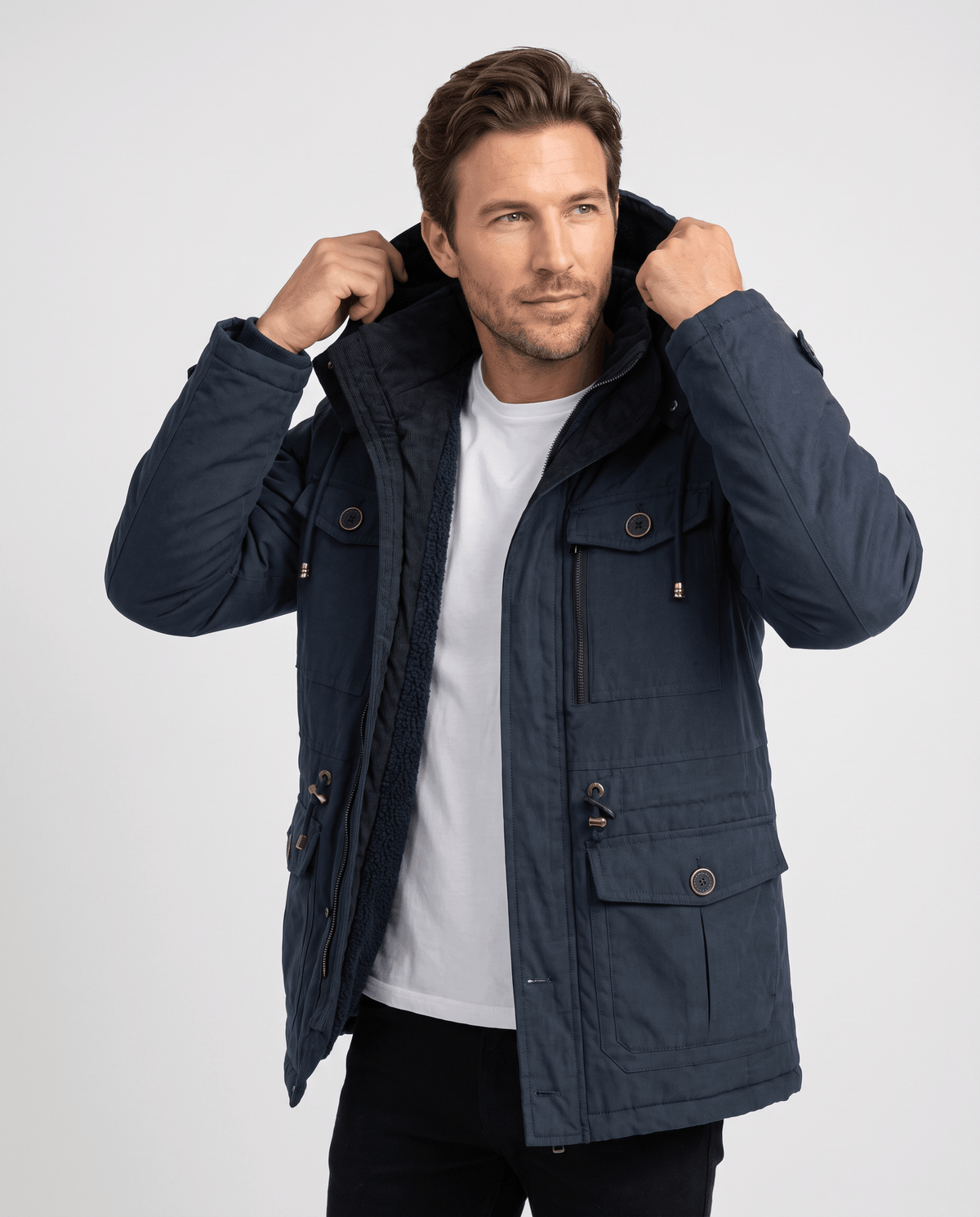 A man wearing a navy blue fleece-lined parka with a detachable hood, insulated design, and multiple utility pockets