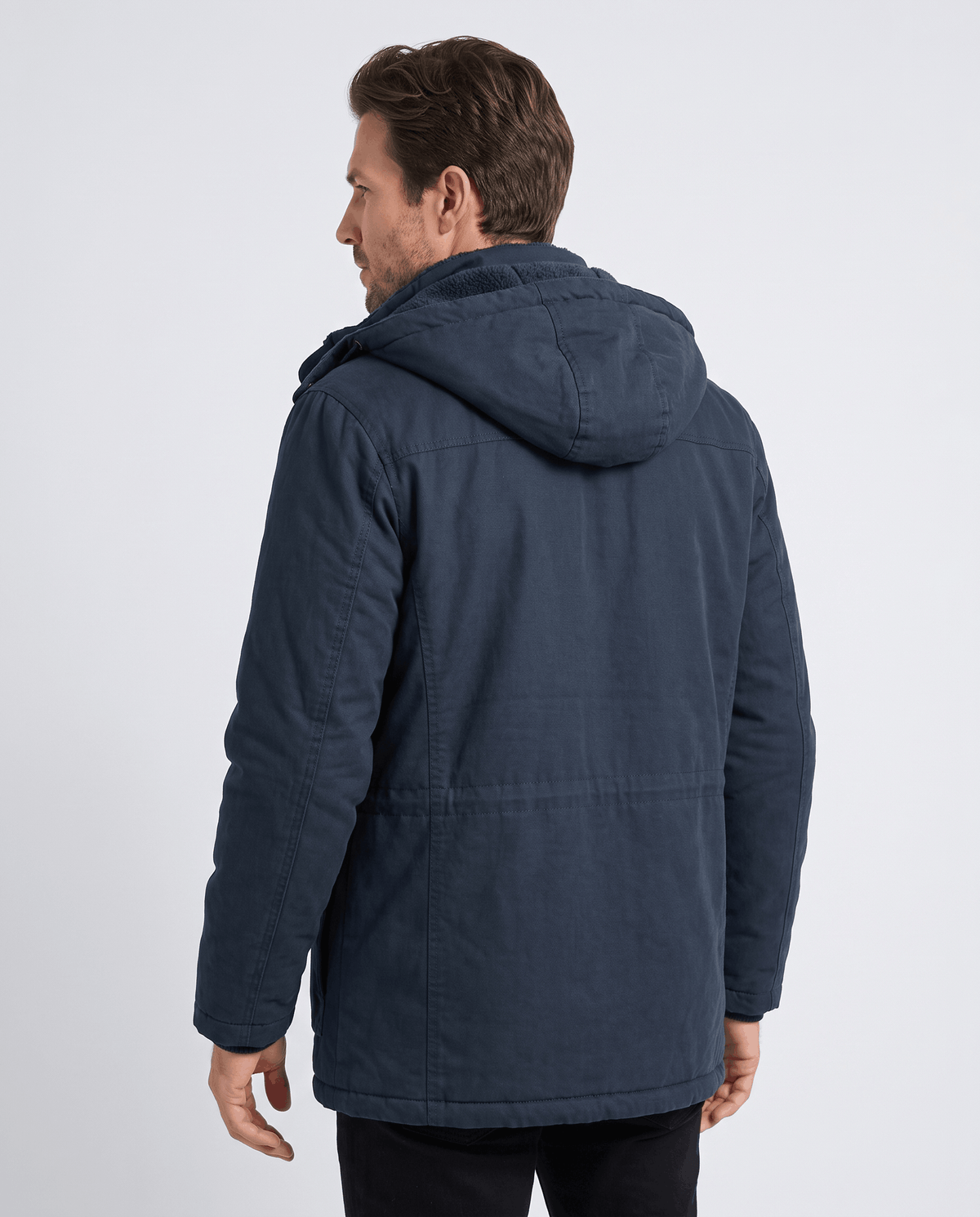 A man wearing a navy blue fleece-lined parka with a detachable hood and insulated design, shown from the back