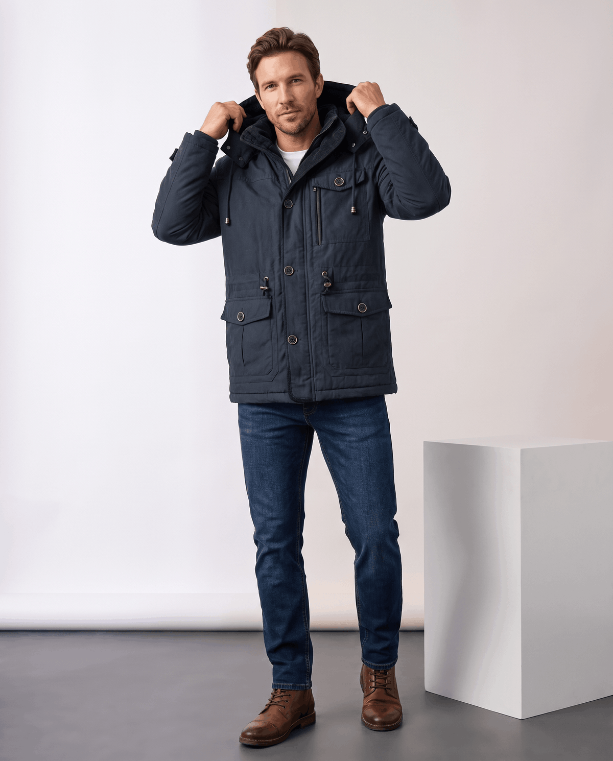 A man wearing a navy blue fleece-lined parka with a detachable hood and insulated design, adjusting the hood