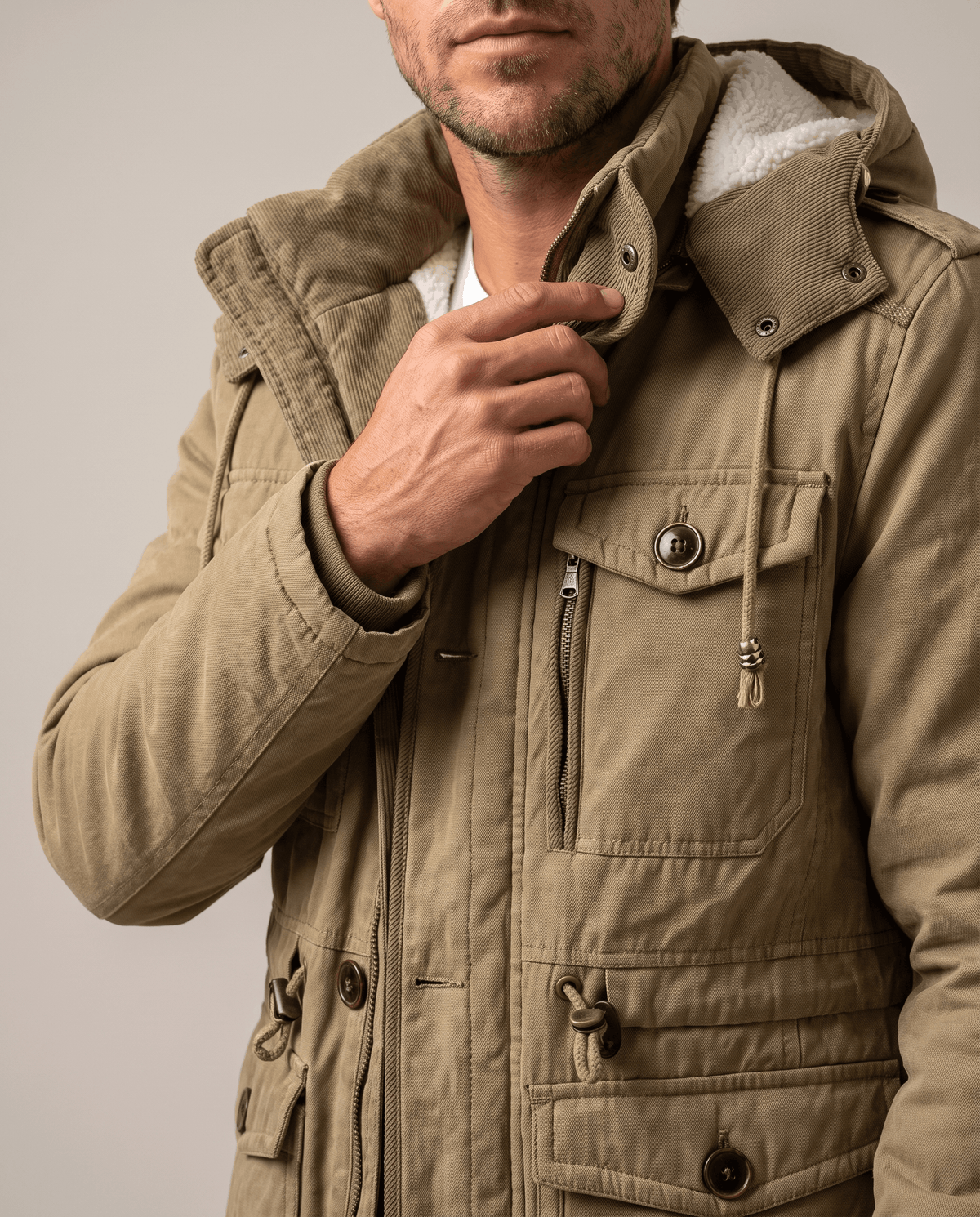 Close-up of a man wearing a beige fleece-lined parka, showing the detachable hood, insulated lining, and front pocket details