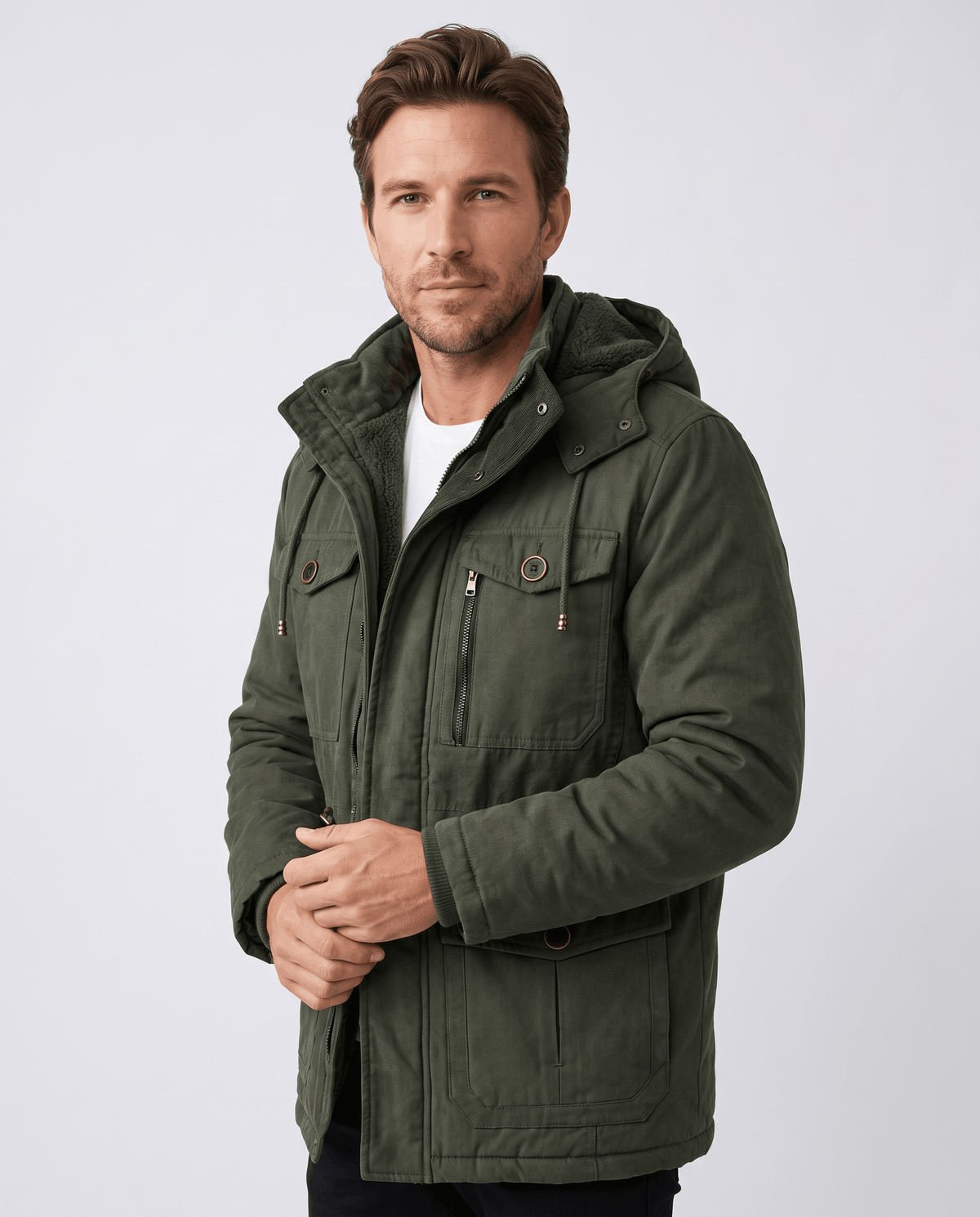 A man wearing a dark green fleece-lined parka with a detachable hood, insulated design, and multiple utility pockets
