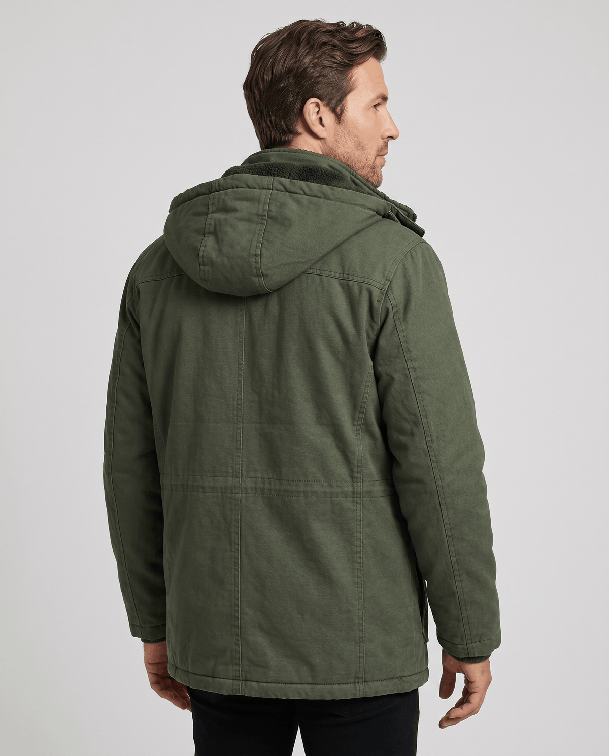 A man wearing a dark green fleece-lined parka with a detachable hood and insulated design, shown from the back