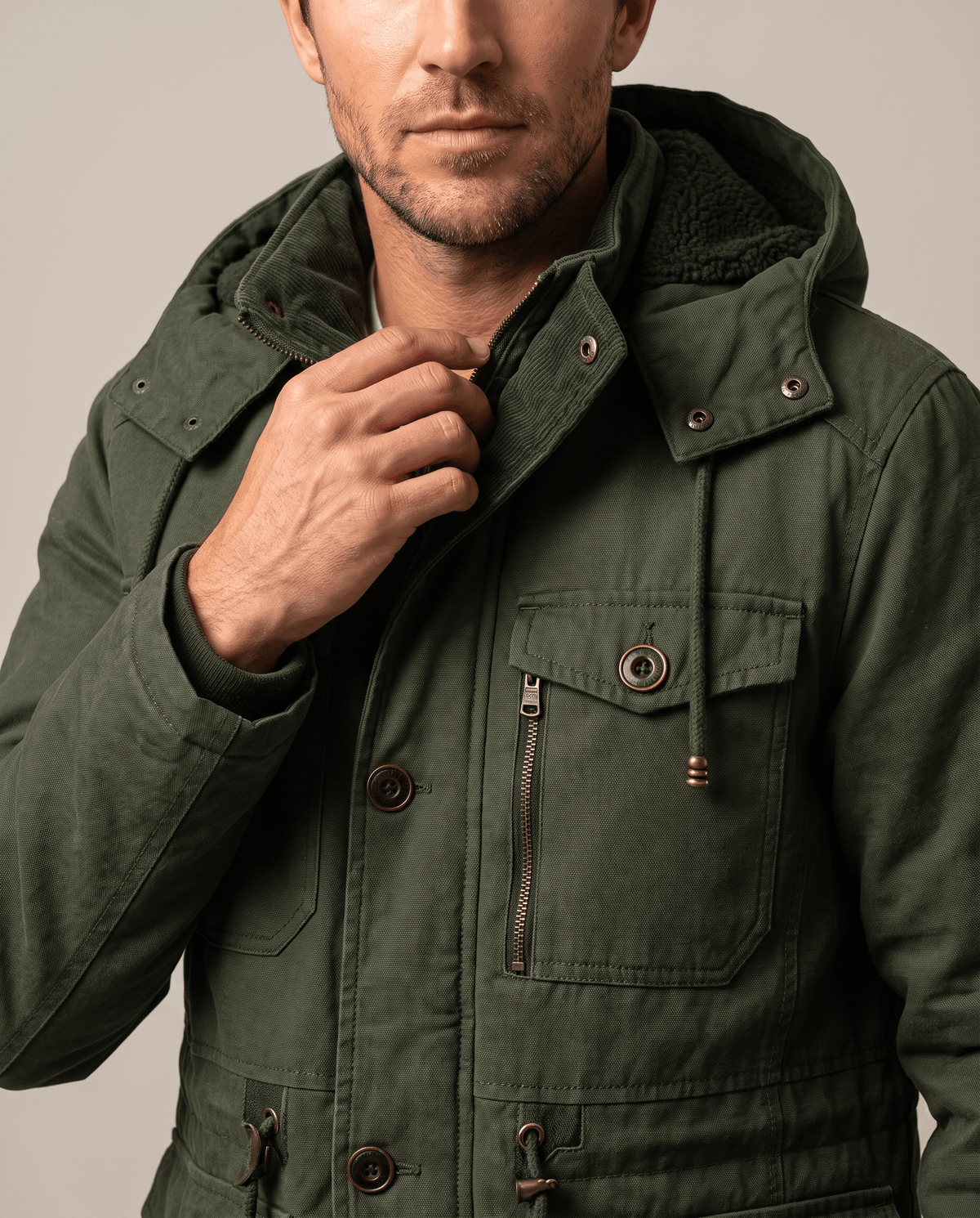 Close-up of a man wearing a dark green fleece-lined parka, showing the detachable hood and front pocket details