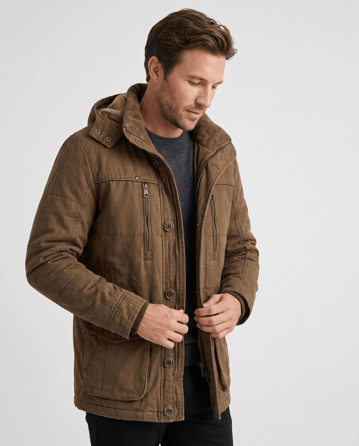 A man wearing a brown fleece-lined parka with an insulated hood and zip front, adjusting the front closure