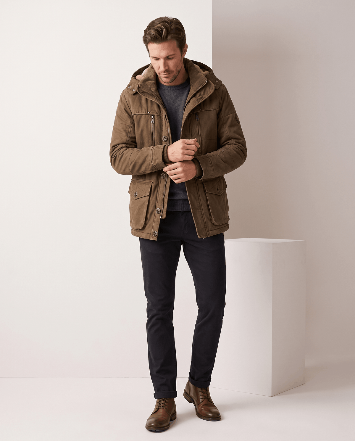 A man wearing a brown fleece-lined parka with an insulated hood and zip front, standing indoors