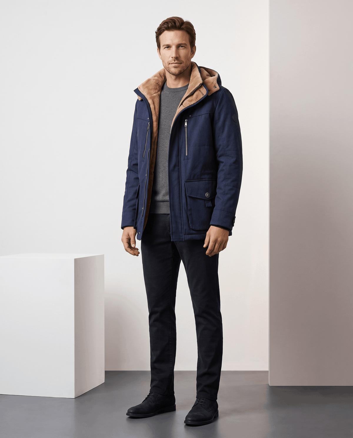 A man wearing a navy blue fleece-lined parka with an insulated hood and zip front, full-body view