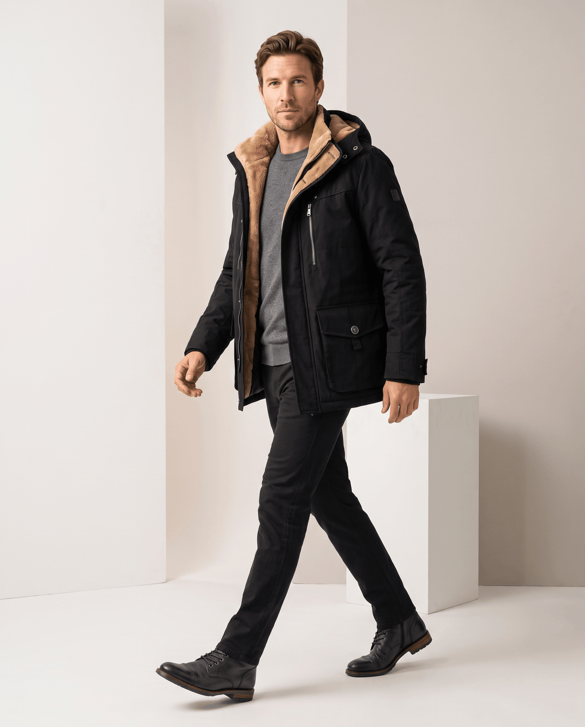 A man wearing a black fleece-lined parka with an insulated hood and zip front, side view