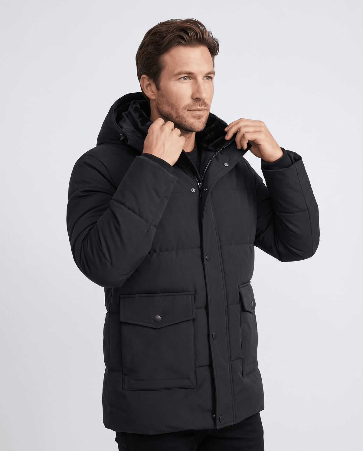 A man wearing a black fleece-lined winter jacket with a hood and full-zip front, adjusting the collar