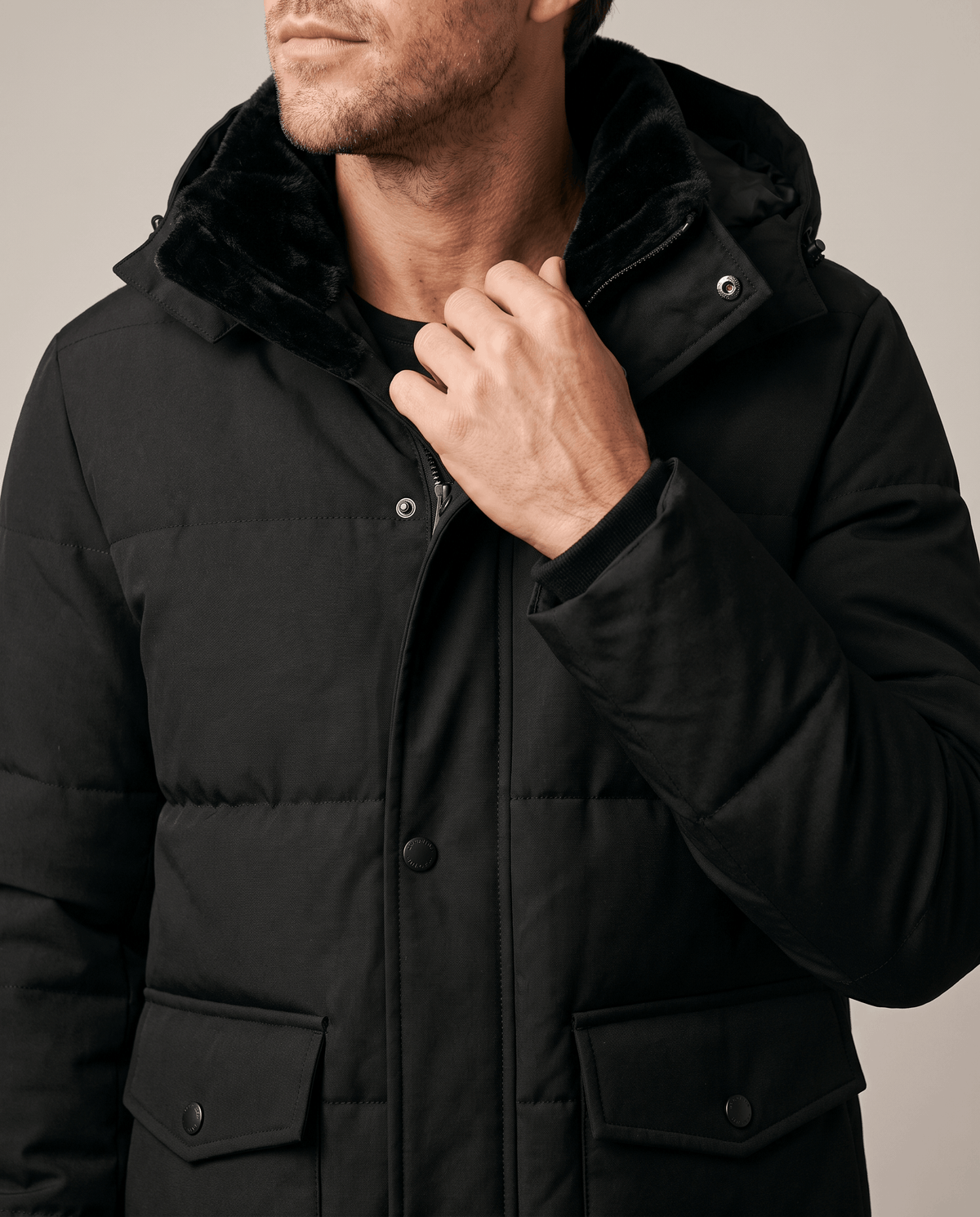 Close-up of a man wearing a black fleece-lined winter jacket, showing the hood, collar, and full-zip front