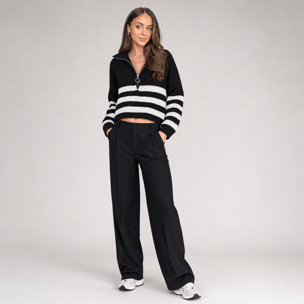 Full-body view of a female model wearing the black and white striped quarter-zip sweater with black trousers.