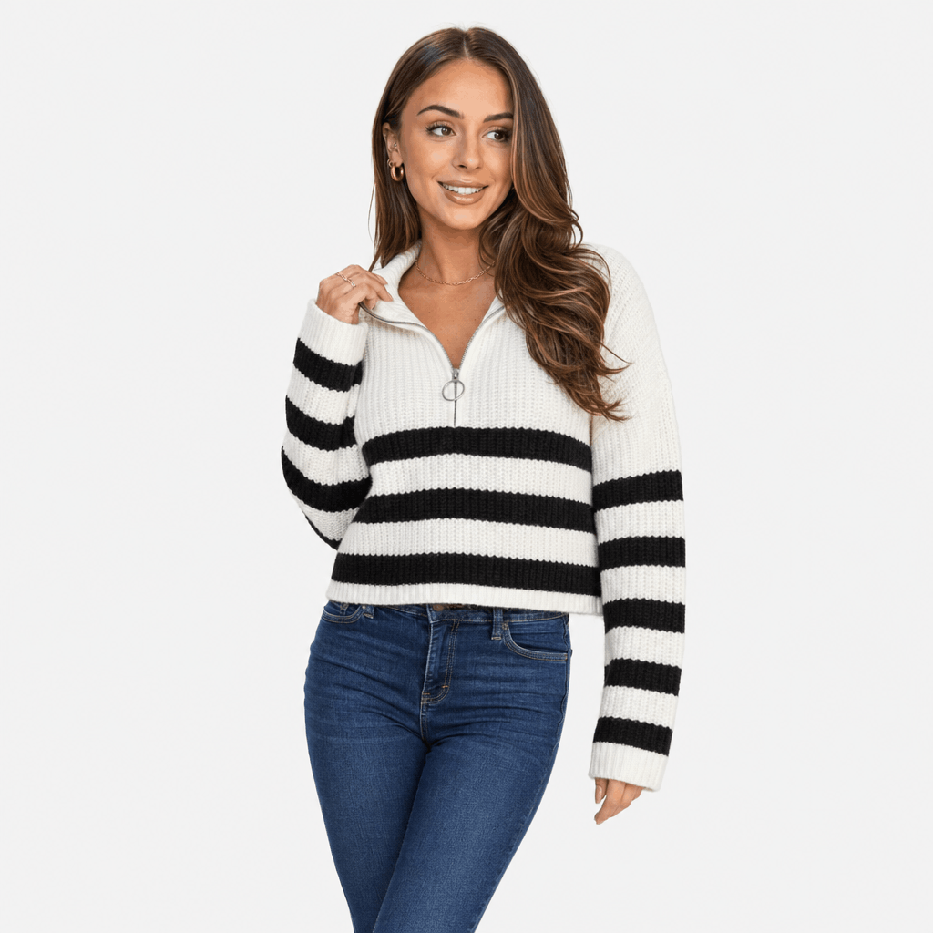 Female model wearing a white quarter-zip sweater with bold black horizontal stripes across the chest and sleeves, paired with blue jeans.