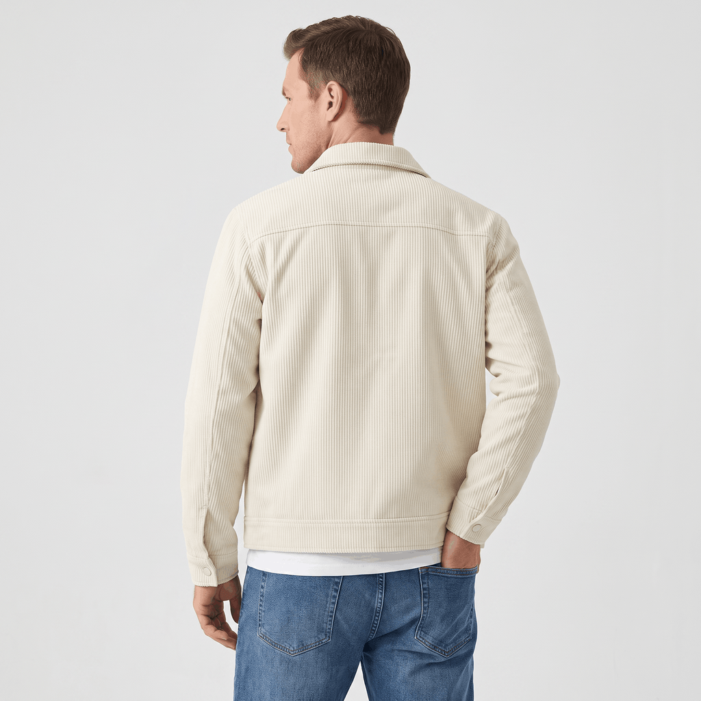 Cream corduroy trucker jacket with a structured collar and clean back yoke, worn over a white tee and blue jeans.