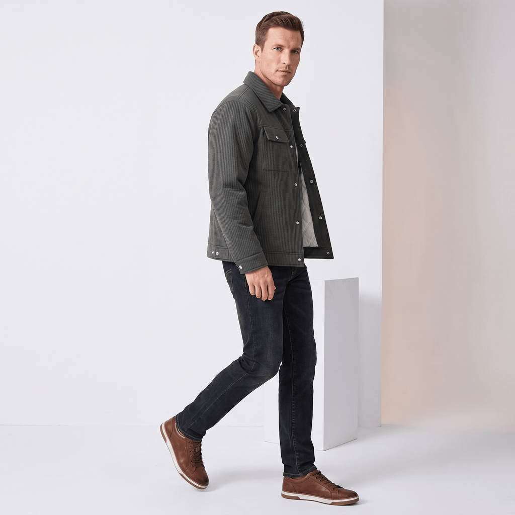 Dark grey corduroy trucker jacket with snap buttons, dual chest pockets, and diamond-quilted lining worn with black jeans.
