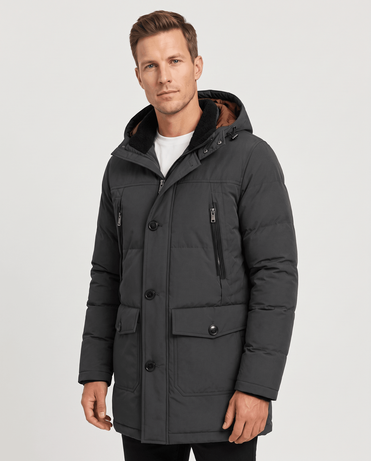 A man wearing a dark gray insulated winter parka with a hood, full-zip front, and multiple utility pockets