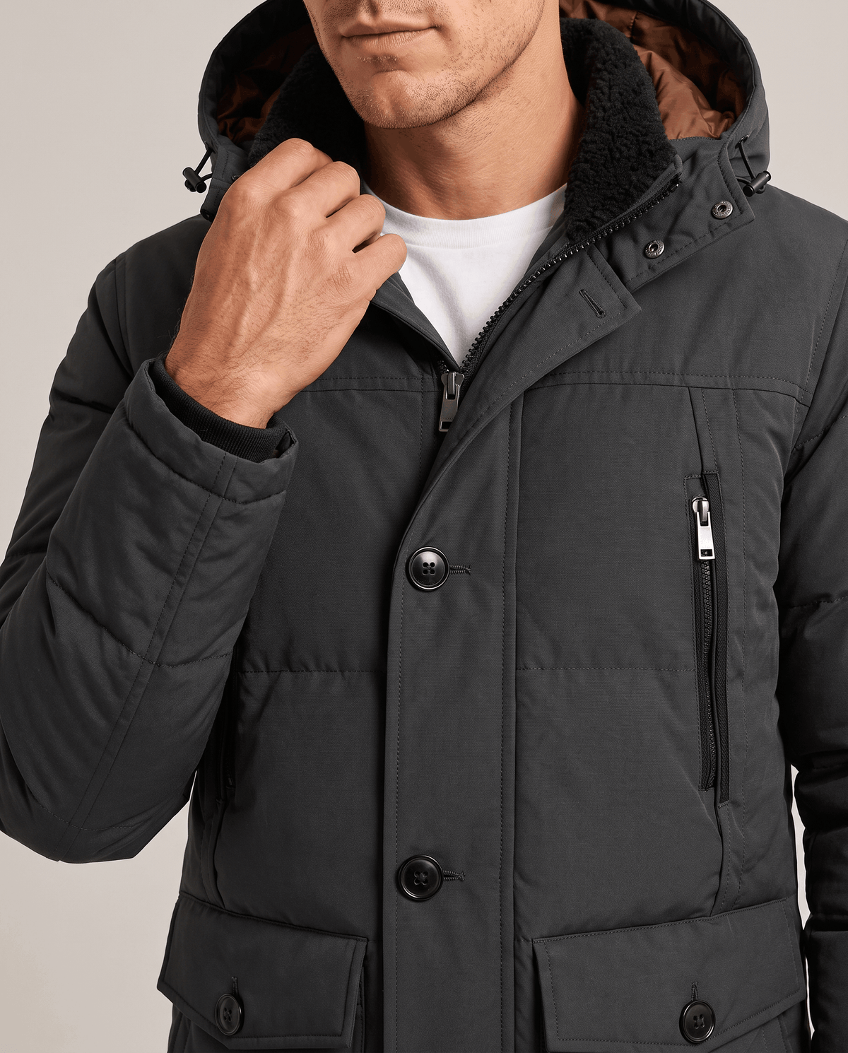 Close-up of a man wearing a dark gray insulated winter parka, showing the hood, front buttons, zipper, and utility pockets