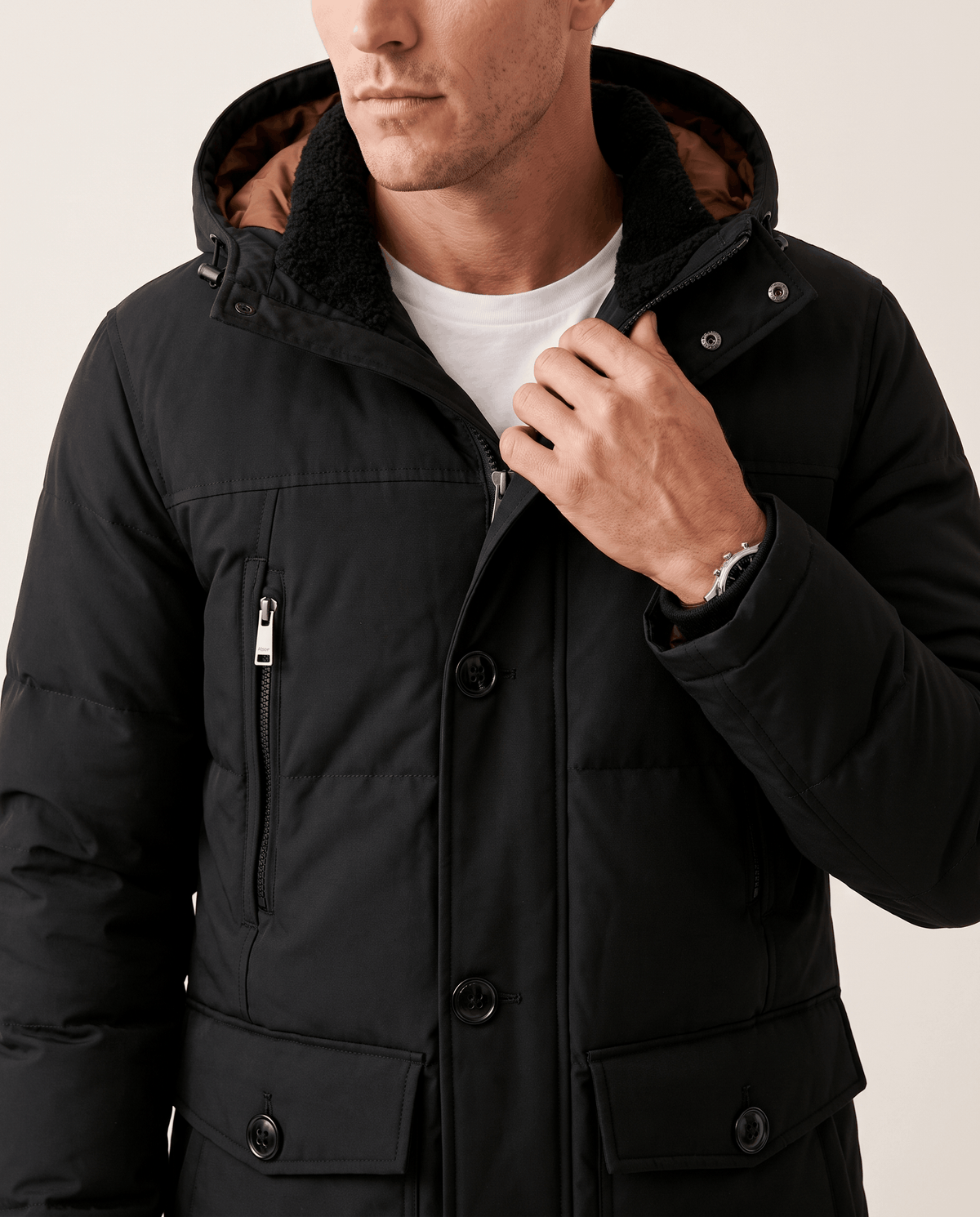 Close-up of a man wearing a black insulated winter parka, showing the hood, front zipper, and utility pockets