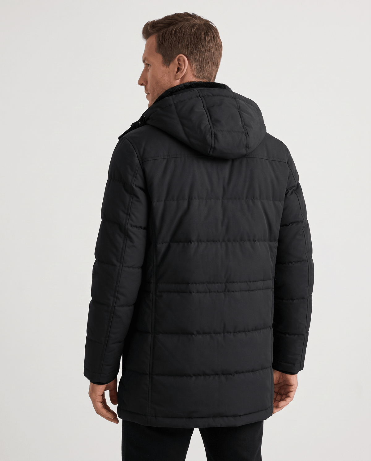 A man wearing a black insulated winter parka with a hood and multiple utility pockets, shown from the back