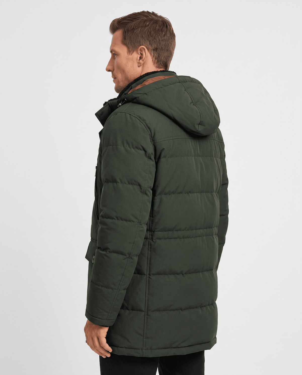 A man wearing a dark green insulated winter parka with a hood and multiple utility pockets, shown from the back