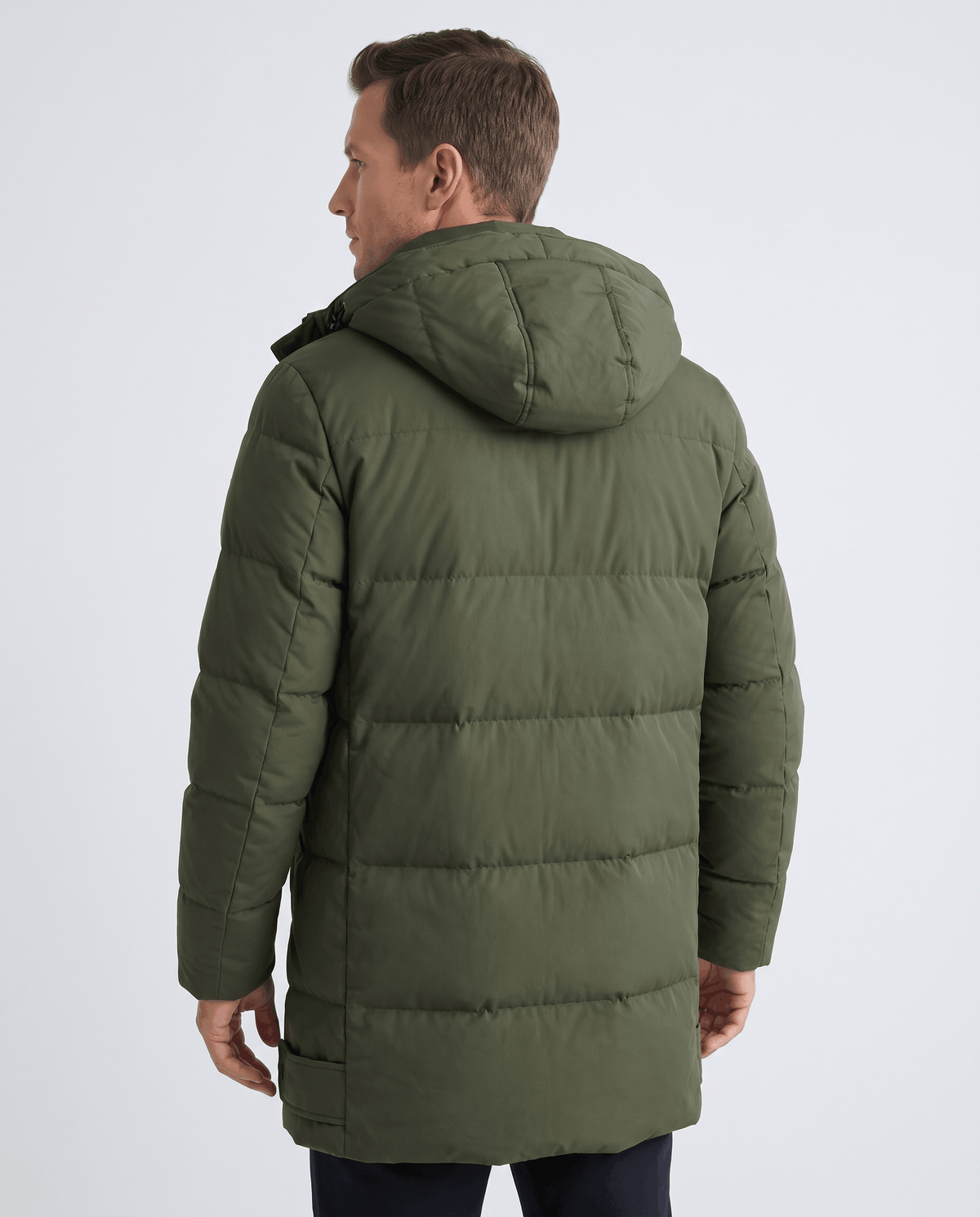 A man wearing an olive green padded longline winter parka with a hood, shown from the back
