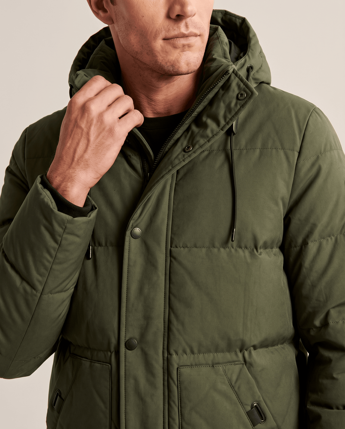 Close-up of a man wearing an olive green insulated winter parka, showing the hood, front closure, and padded shell