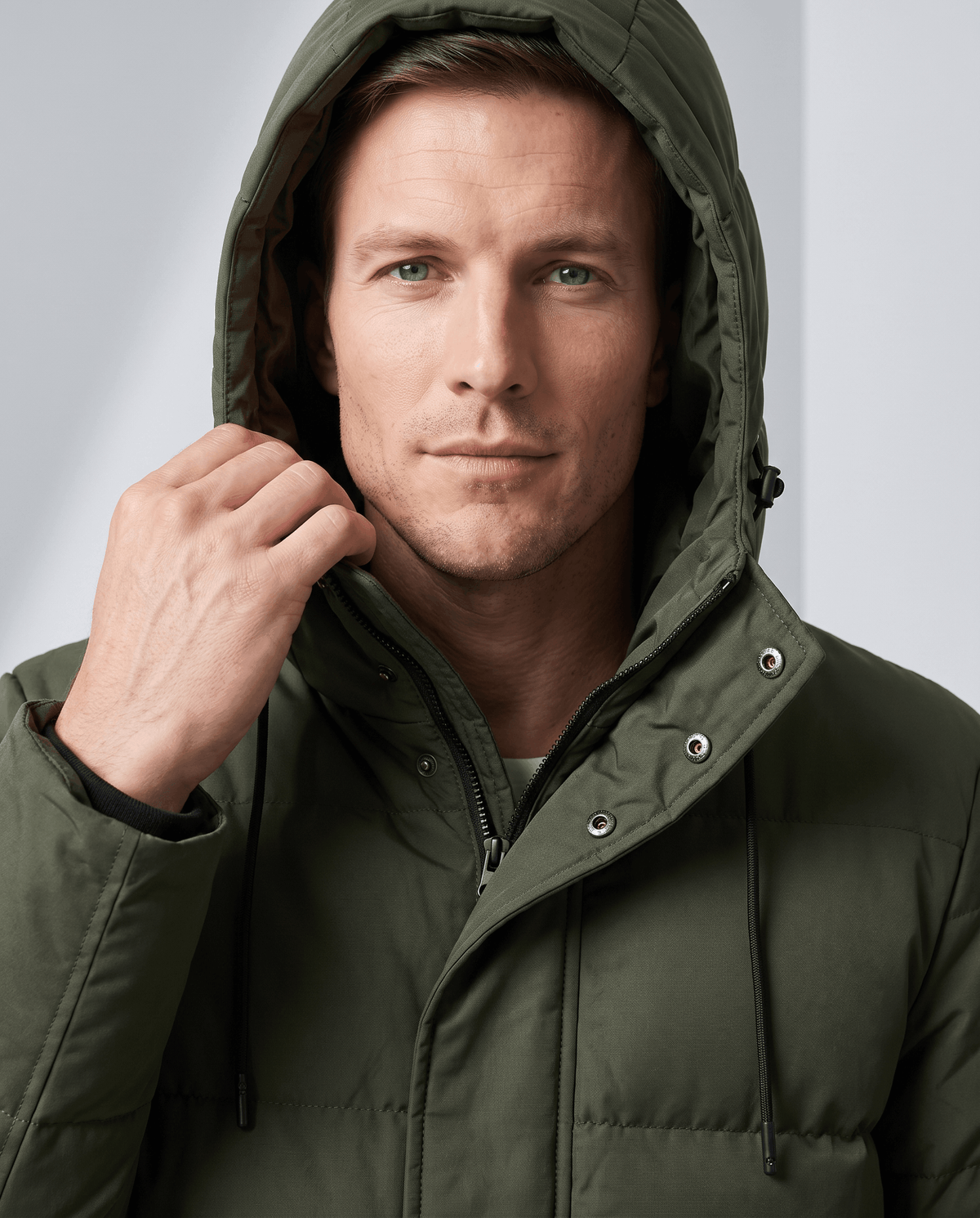 Close-up of a man wearing an olive green insulated winter parka, showing the hood and water-resistant shell
