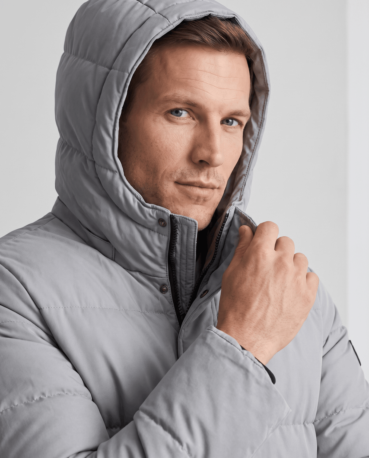 Close-up of a man wearing a light gray insulated winter parka, showing the hood and padded shell
