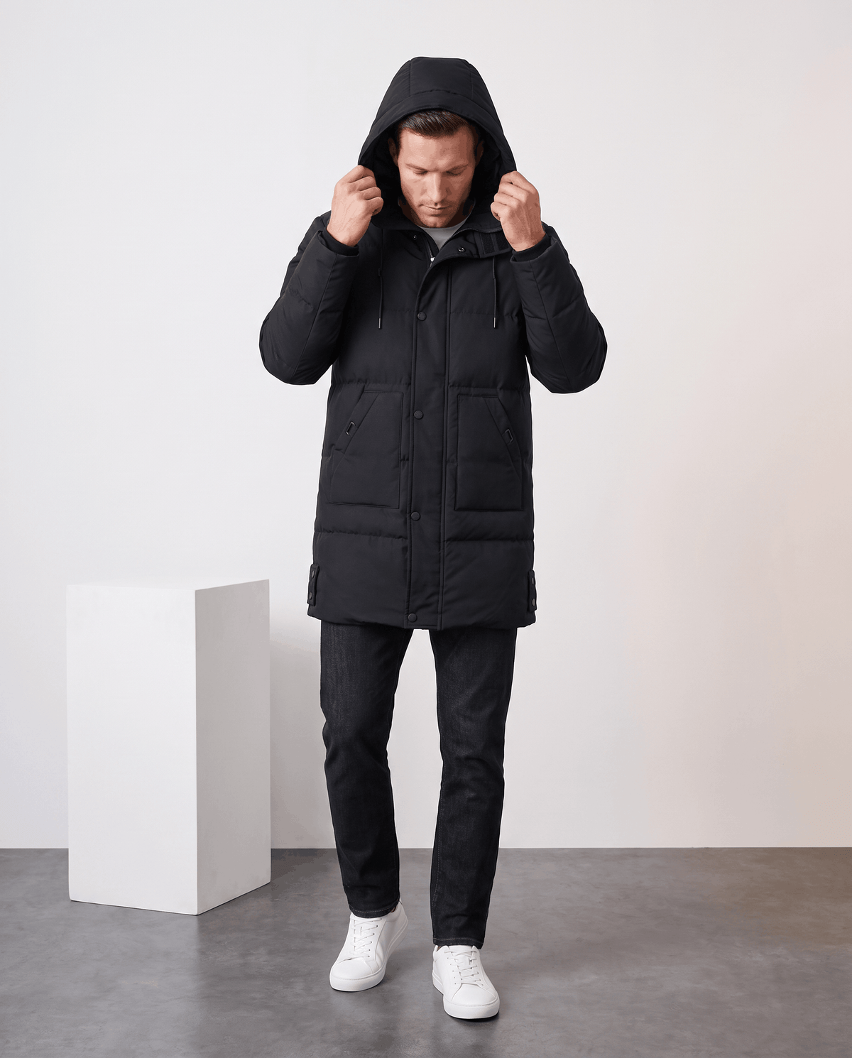 A man wearing a black insulated winter parka with a hood, standing indoors