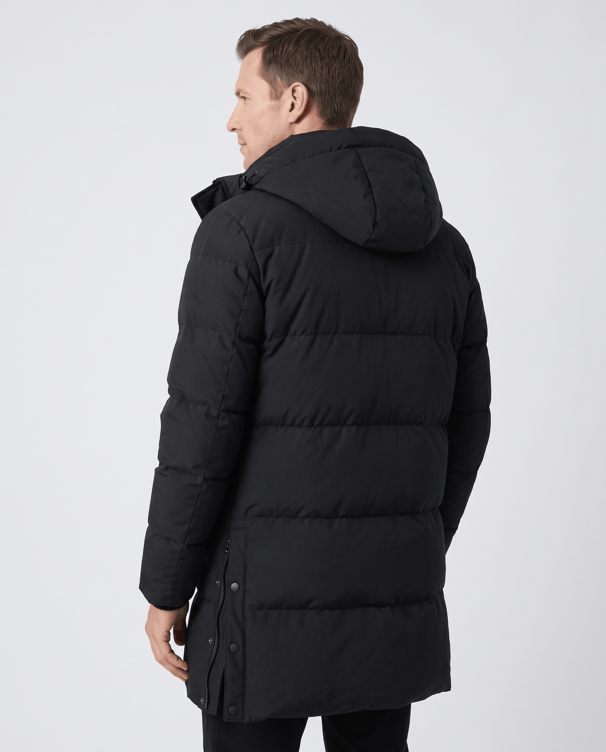 A man wearing a black padded longline winter parka with a hood, shown from the back