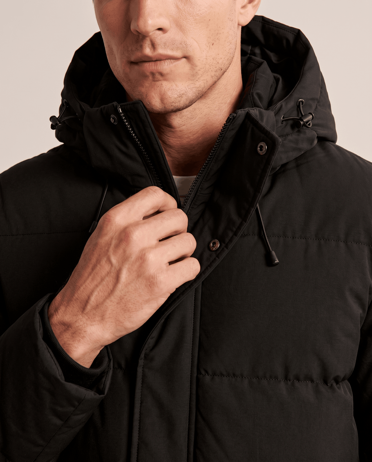 Close-up of a man wearing a black insulated winter parka, showing the hood, front closure, and padded design
