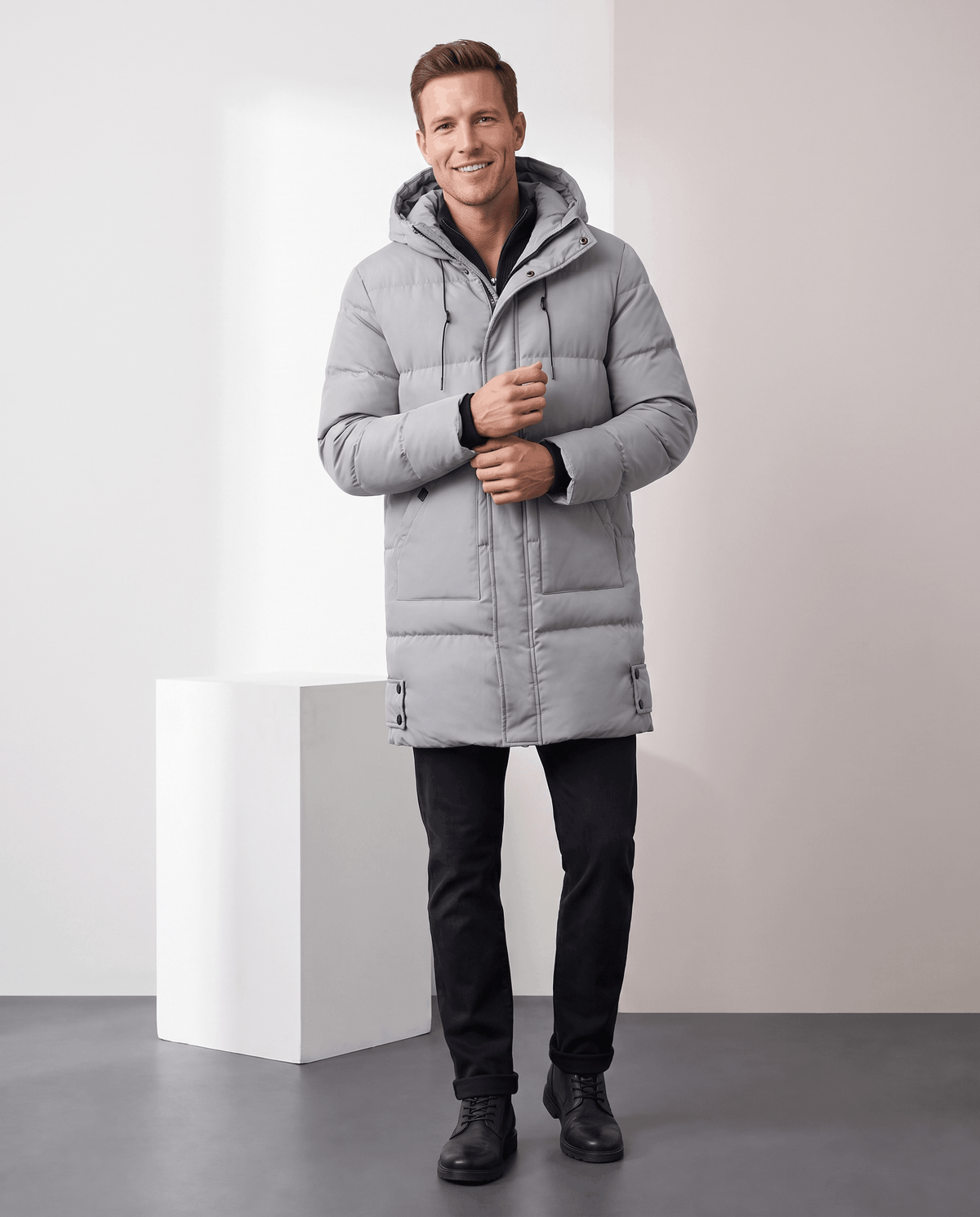 A man wearing a light gray insulated winter parka with a water-resistant shell, padded longline design, and hood