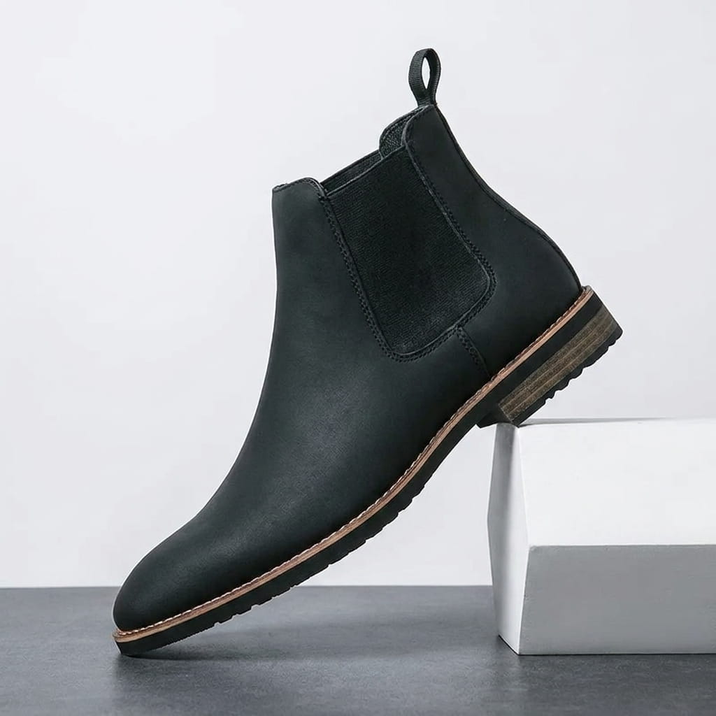 Black Chelsea boot with an elastic side panel, rear pull tab, smooth leather-style upper, and rugged lug sole.