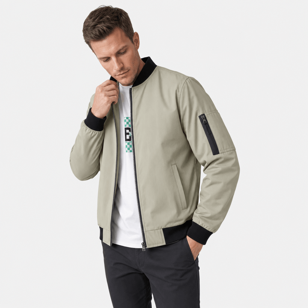 Man wearing a light beige bomber jacket over a dark shirt, posing with one hand near his face.