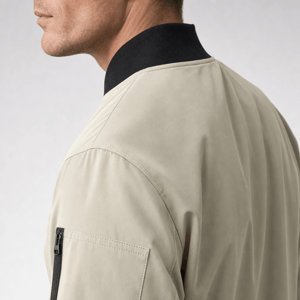 Back and shoulder close-up of a light beige bomber jacket with a dark ribbed collar.