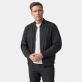 Man wearing a black bomber jacket over a white T-shirt and black trousers, standing against a light studio background.