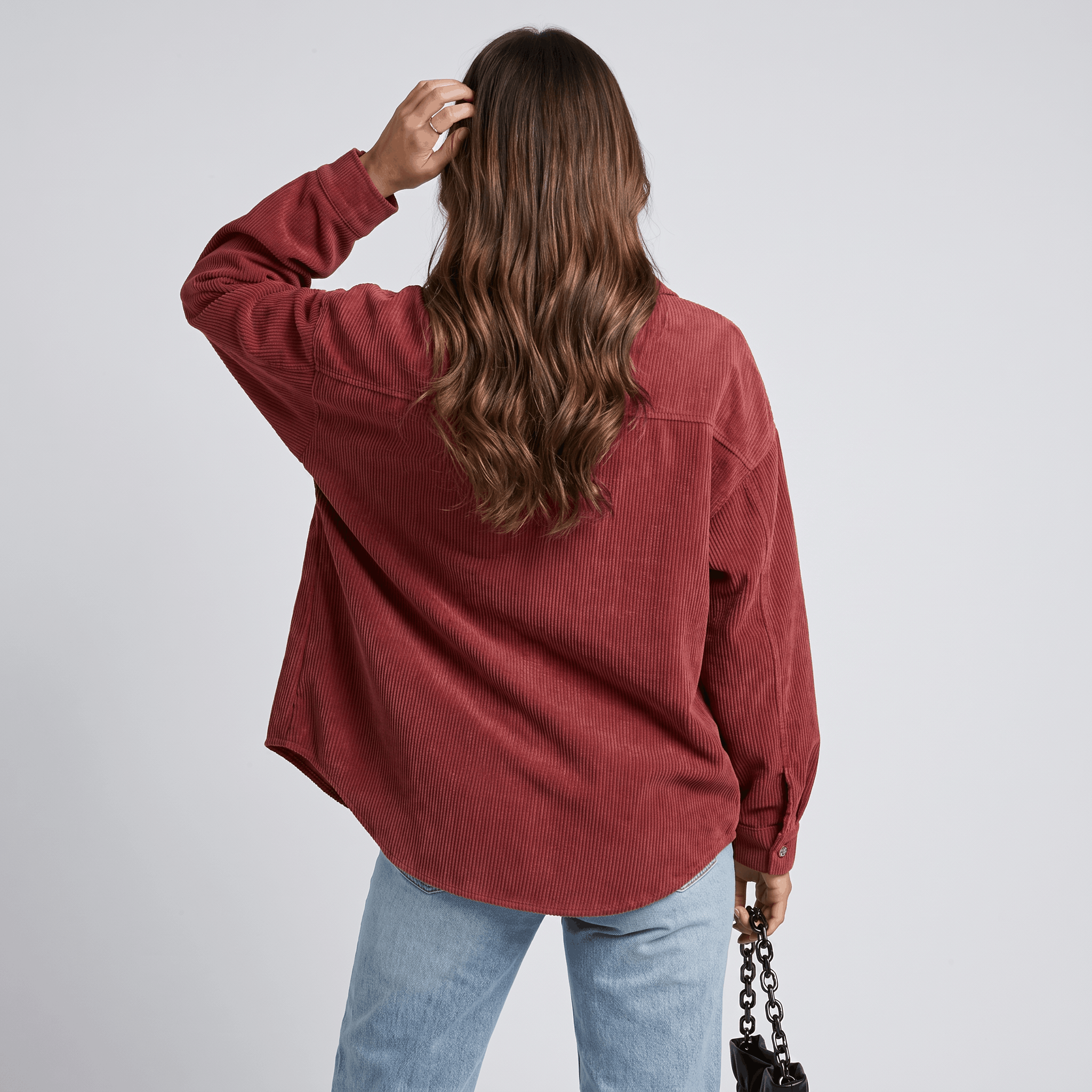 Rust-toned oversized corduroy button-down shirt with a drop-shoulder fit and ribbed texture, worn with light-wash jeans.