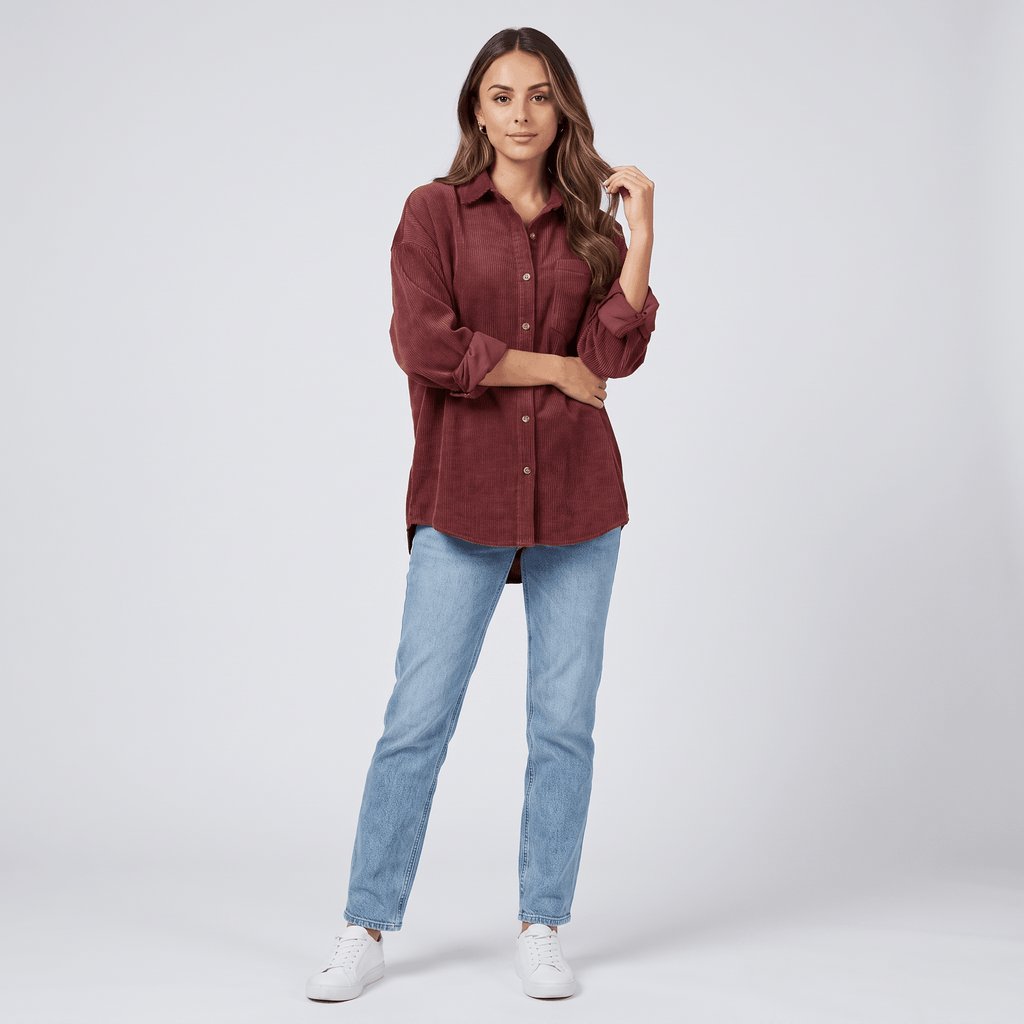 Oversized rust corduroy button-down shirt with drop shoulders and point collar, styled with light wash straight-leg jeans.