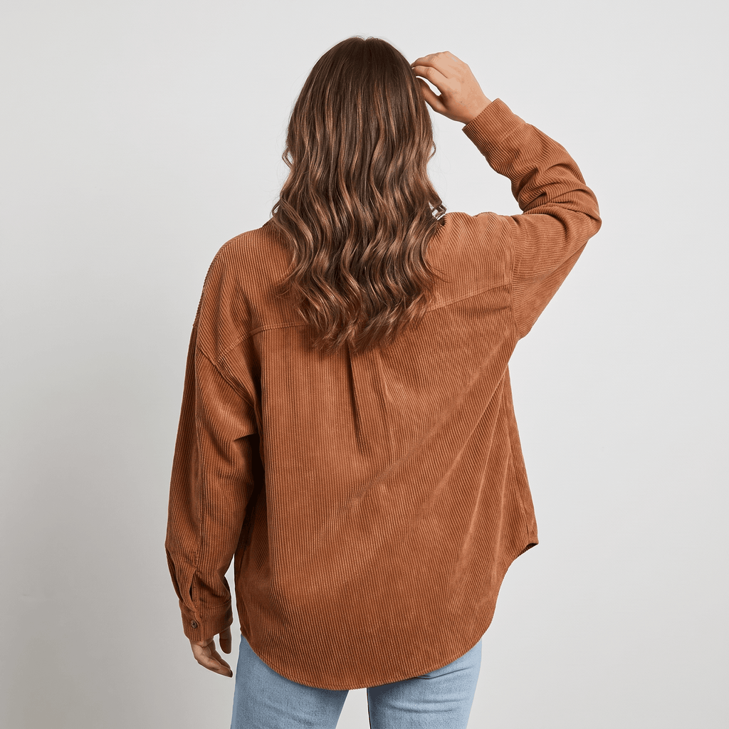 Rust-toned corduroy button-down shirt with an oversized, drop-shoulder fit and fine ribbed texture worn with blue jeans.
