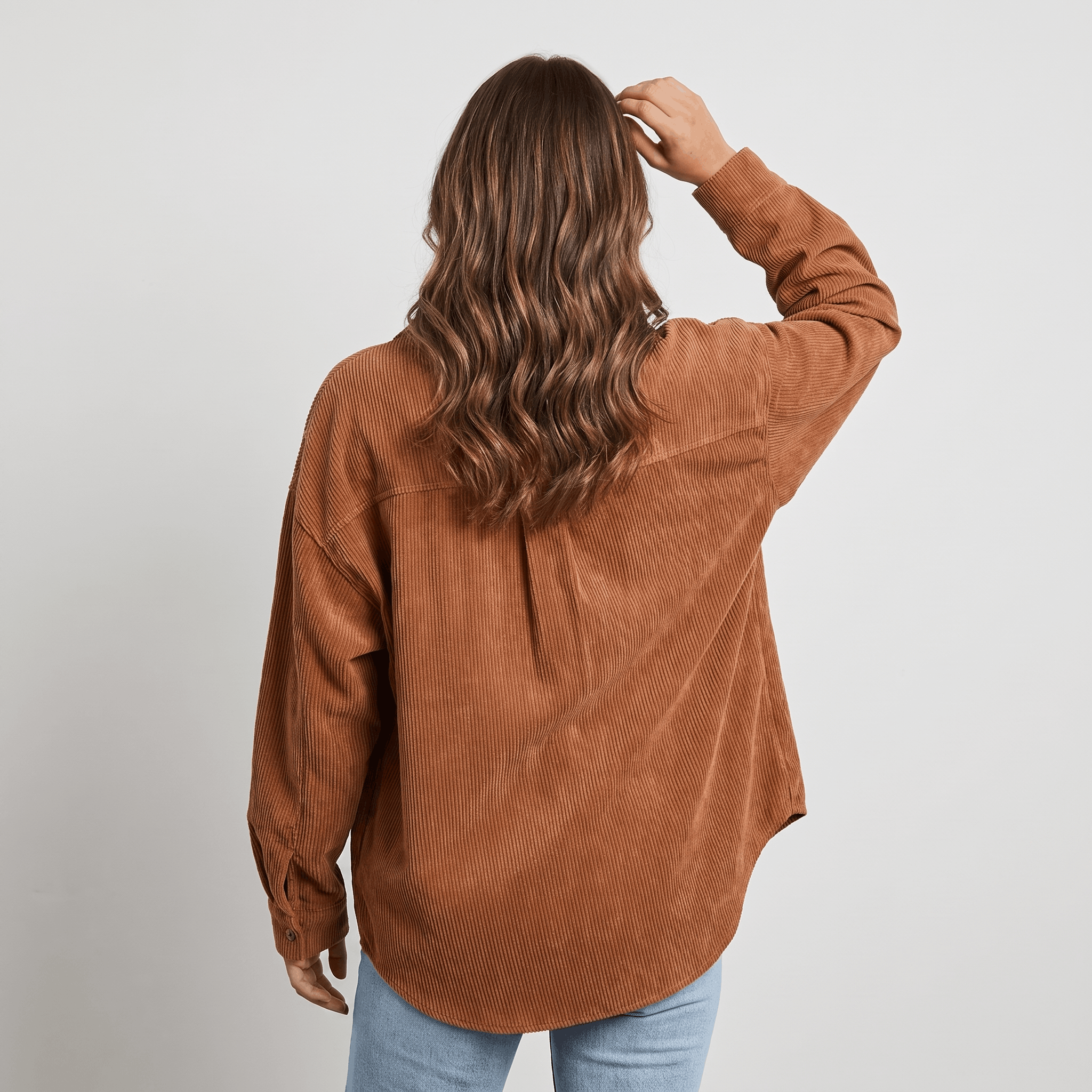 Rust-toned corduroy button-down shirt with an oversized, drop-shoulder fit and fine ribbed texture worn with blue jeans.