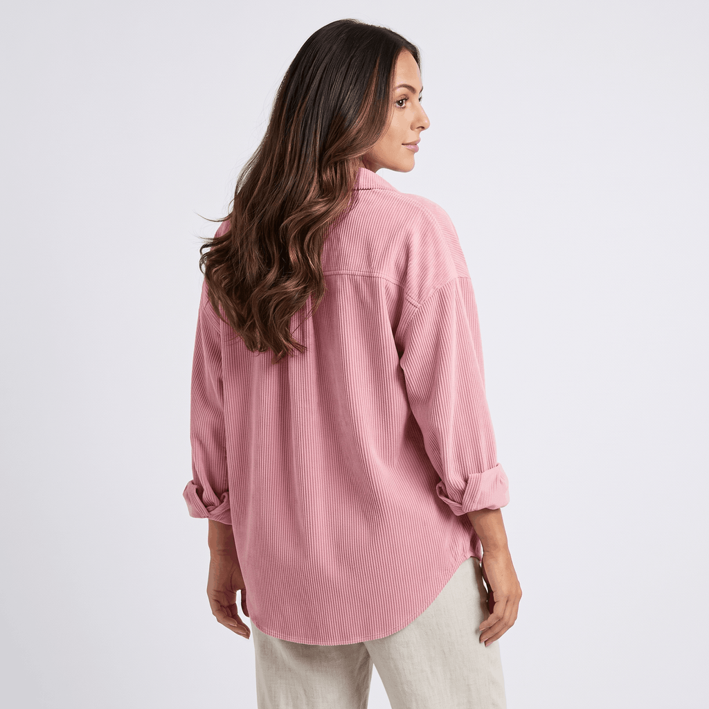 Oversized pink corduroy button-down shirt with drop shoulders and rolled cuffs, worn untucked over neutral trousers.