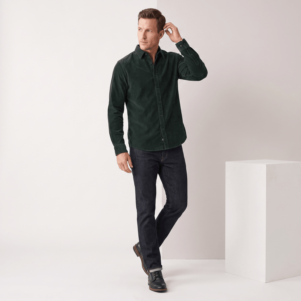 Slim-fit dark green corduroy shirt with a clean, pocketless front and classic collar, styled with dark denim jeans.
