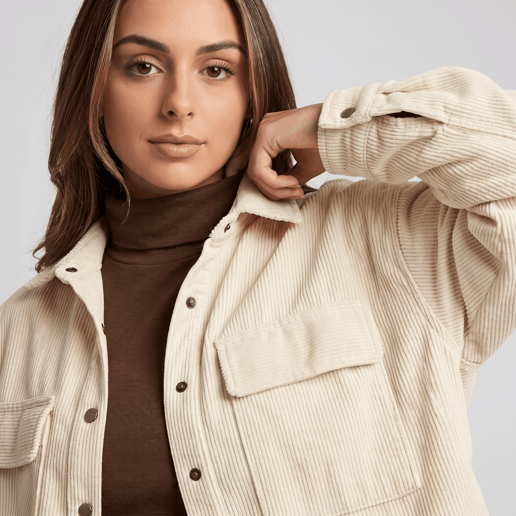 Oversized khaki wide wale corduroy shirt jacket with buttoned chest pockets layered over a brown turtleneck.