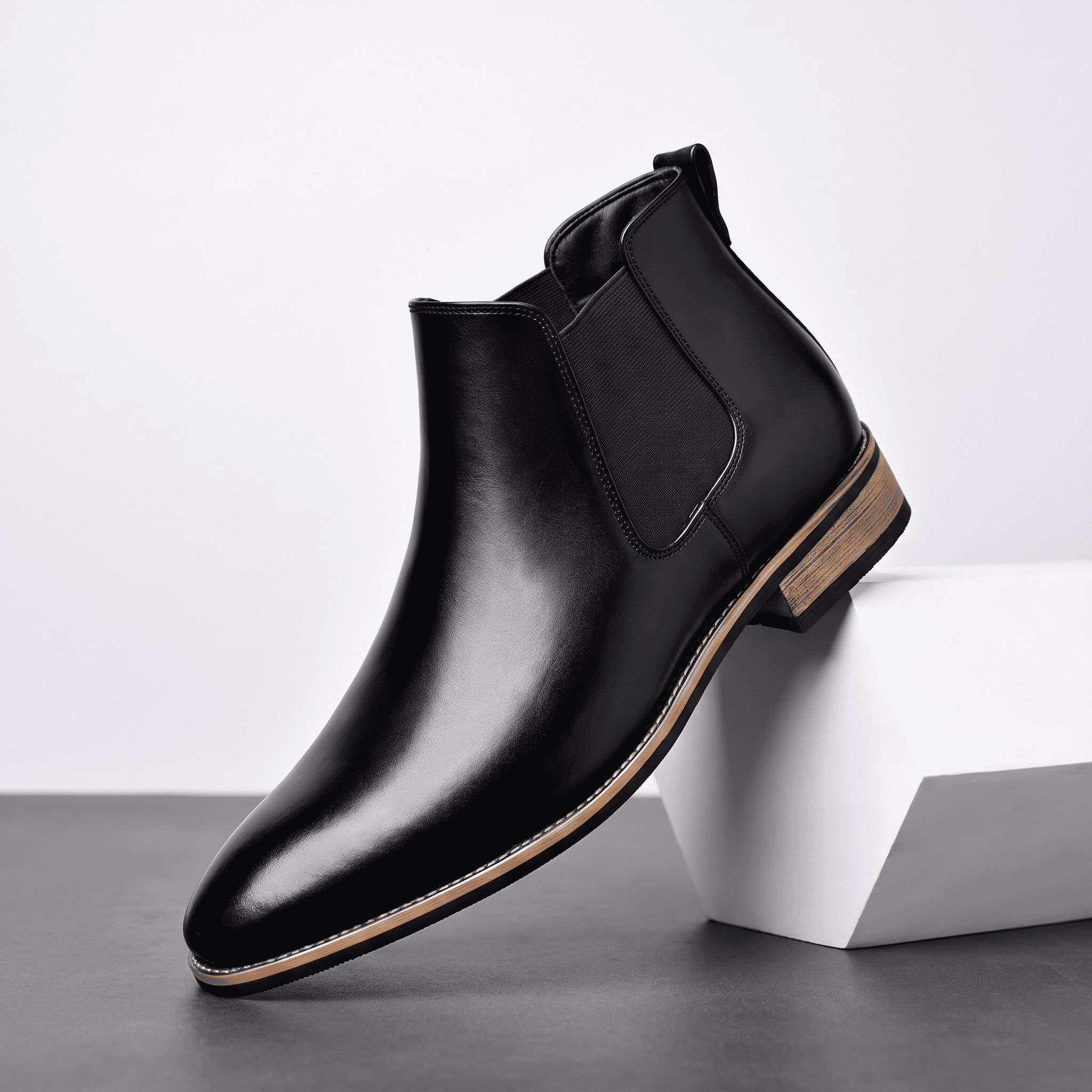 Single black leather Chelsea boot displayed on a white pedestal, showing the smooth upper and low stacked heel.
