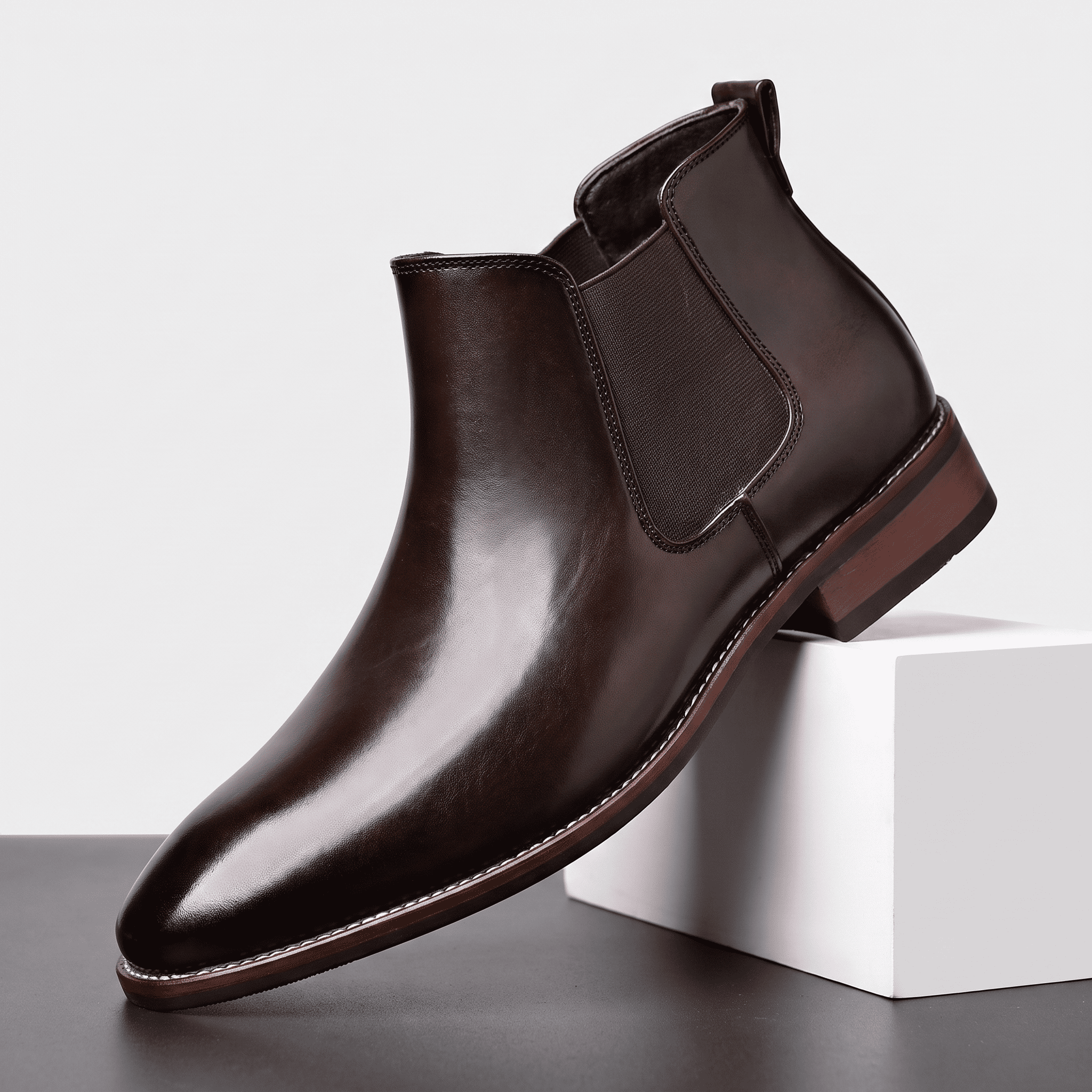 Single black leather Chelsea boot displayed on a white pedestal, featuring an elastic side panel, pull tab, and low stacked heel.